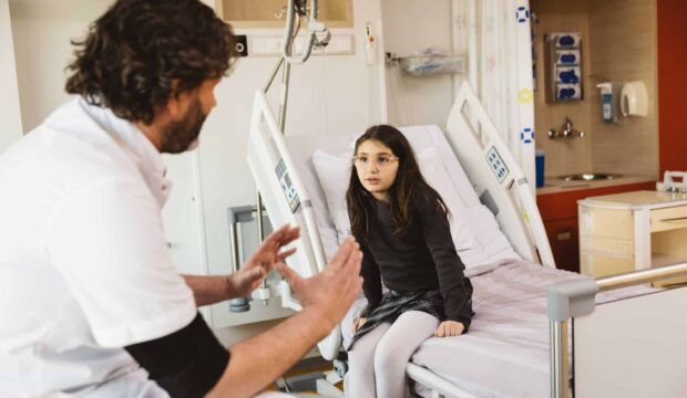 Meisje zittend op bed, luisterend naar de arts die uitleg geeft.